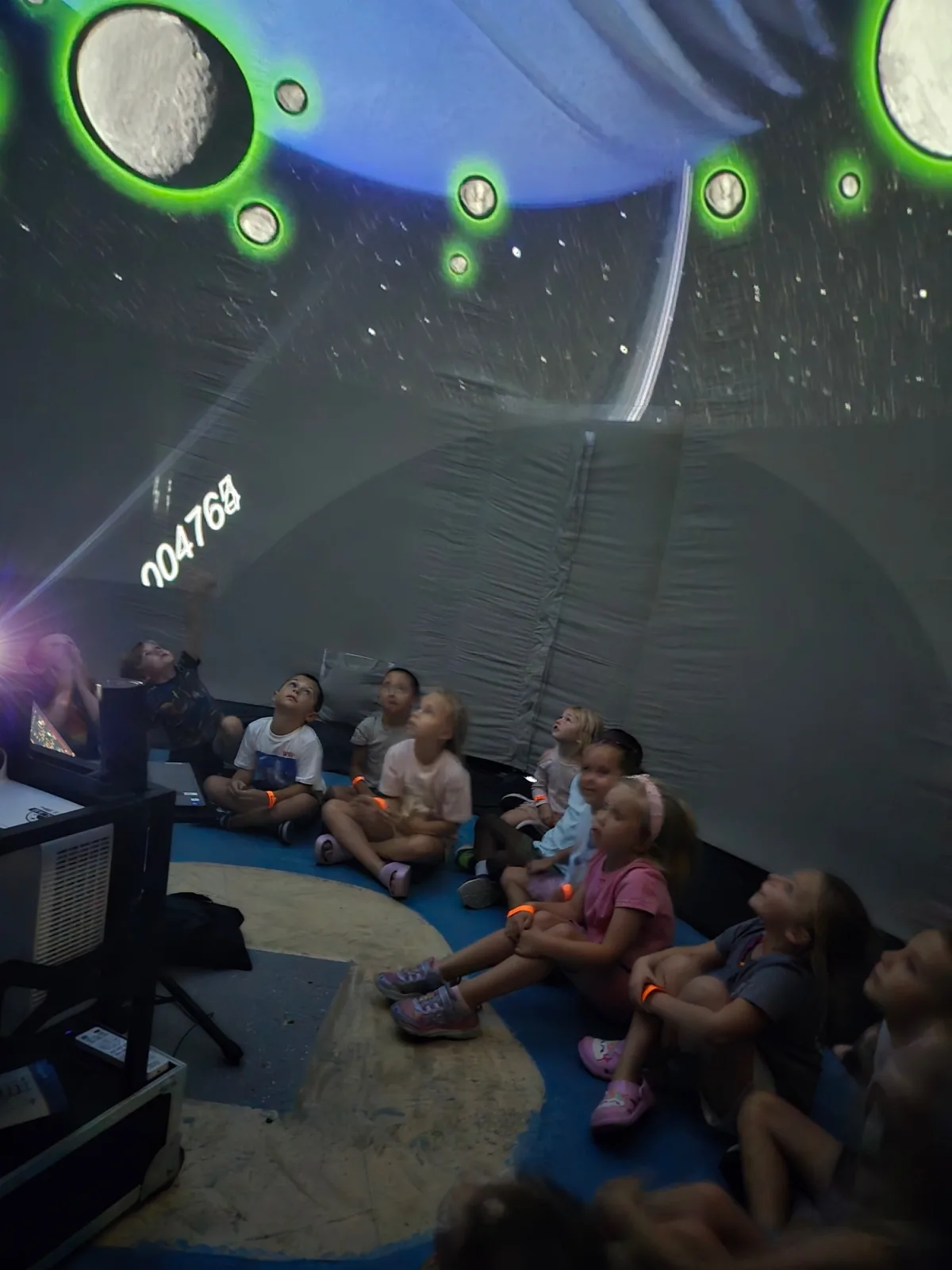 Children seated inside the inflatable planetarium look up at moons and planets projected on the dome