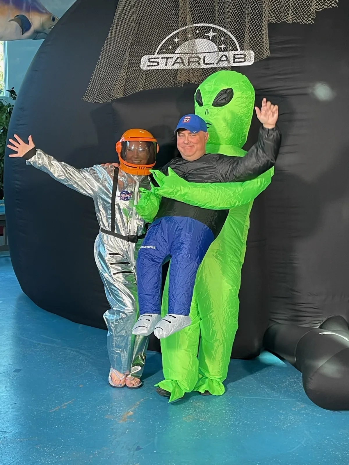 Two people in an astronaut costume and an inflatable alien costume pose in front of the STARLAB planetarium dome